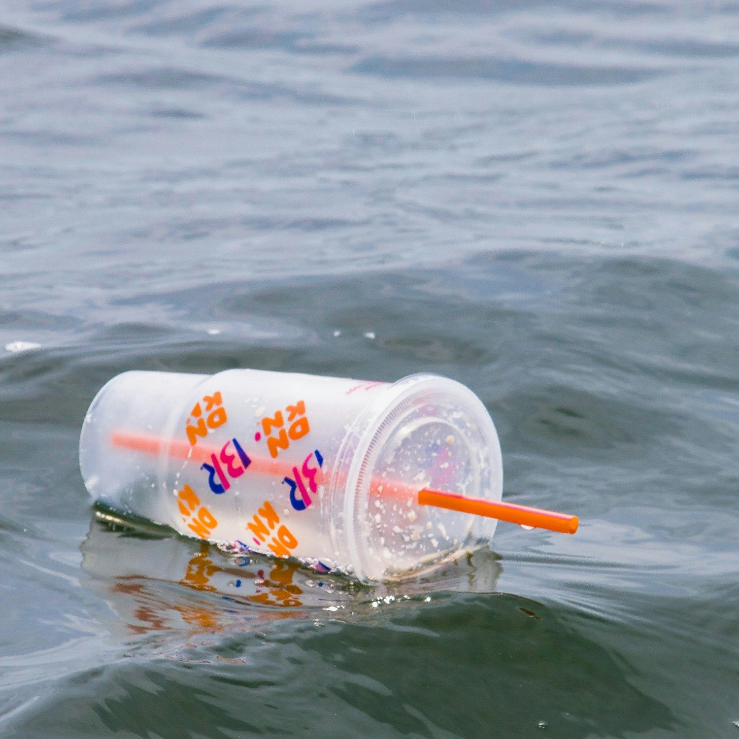 Plastic cup with a straw floating on water